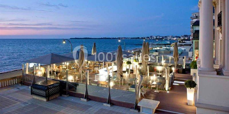 Terrasse d'un restaurant en bord de mer au crépuscule, avec éclairage chaleureux et vue sur l'océan.