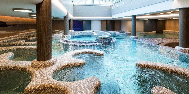 Bassin intérieur avec jets d'eau, colonnes et mosaïques, éclairé par une verrière.