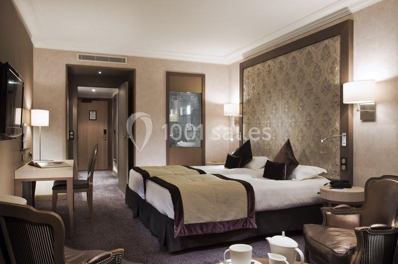 Chambre d'hôtel avec deux lits simples, bureau, fauteuils en cuir et éclairage doux dans un décor élégant.