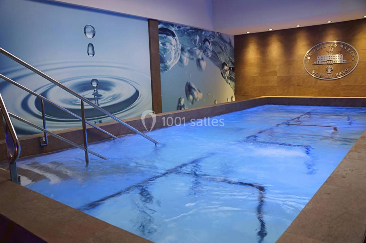 Piscine intérieure éclairée en bleu avec des rampes métalliques, décorée de panneaux muraux sur le thème de l'eau.