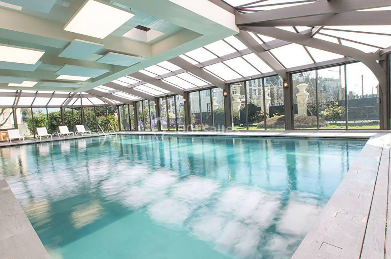 Piscine intérieure lumineuse avec baies vitrées donnant sur un jardin.