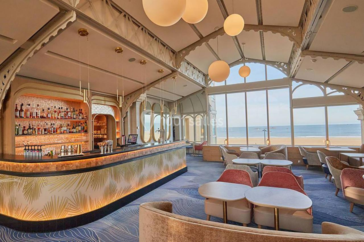 Intérieur d'un bar élégant avec vue sur la mer, grandes baies vitrées, mobilier moderne et éclairage chaleureux.