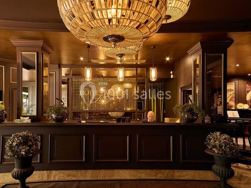 Réception d'un hôtel élégant avec un comptoir sombre, des lustres imposants et une décoration raffinée.