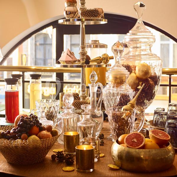 Table décorée avec des carafes en verre, des fruits, des bougies et des éléments dorés dans un cadre lumineux.