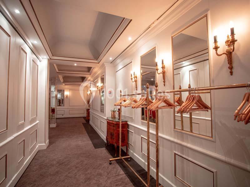 Couloir élégant avec murs blancs ornés de moulures, miroirs, appliques dorées et portants avec cintres en bois.