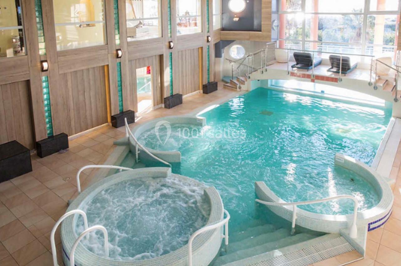 Piscine intérieure avec jets d'eau, bains à remous et chaises longues dans un espace lumineux en bois et verre.