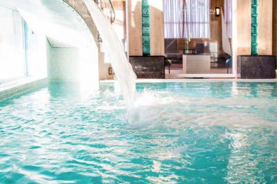 Chambre lumineuse avec un canapé rose, un lit double aux coussins jaunes et une table décorée de fleurs.