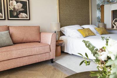 Chambre lumineuse avec un canapé rose, un lit double aux coussins jaunes et une table décorée de fleurs.