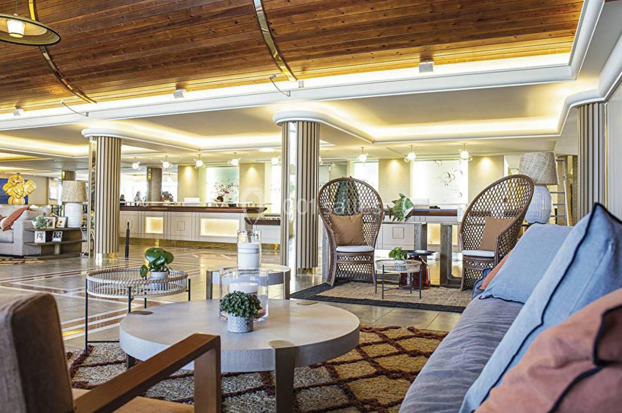 Espace intérieur lumineux avec mobilier moderne, fauteuils en rotin, tables basses et plafond en bois.