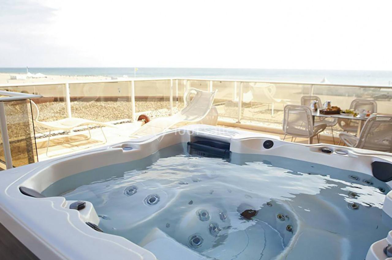 Jacuzzi extérieur sur une terrasse avec vue sur la mer, entouré de chaises et d'une barrière en verre.