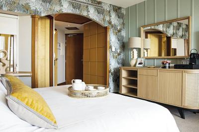 Chambre lumineuse avec un canapé rose, un lit double aux coussins jaunes et une table décorée de fleurs.