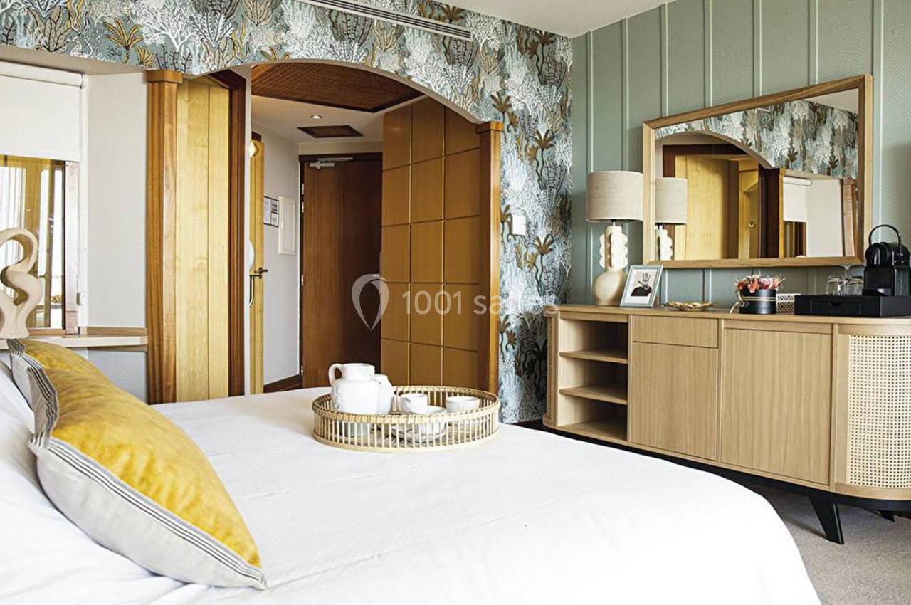 Chambre lumineuse avec lit, commode en bois, plateau de service et décoration murale végétale.