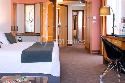 Chambre lumineuse avec un canapé rose, un lit double aux coussins jaunes et une table décorée de fleurs.