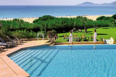 Chambre lumineuse avec un canapé rose, un lit double aux coussins jaunes et une table décorée de fleurs.