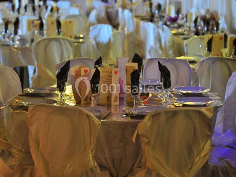 Tables rondes décorées avec nappes blanches, serviettes noires et menus, prêtes pour un événement festif.