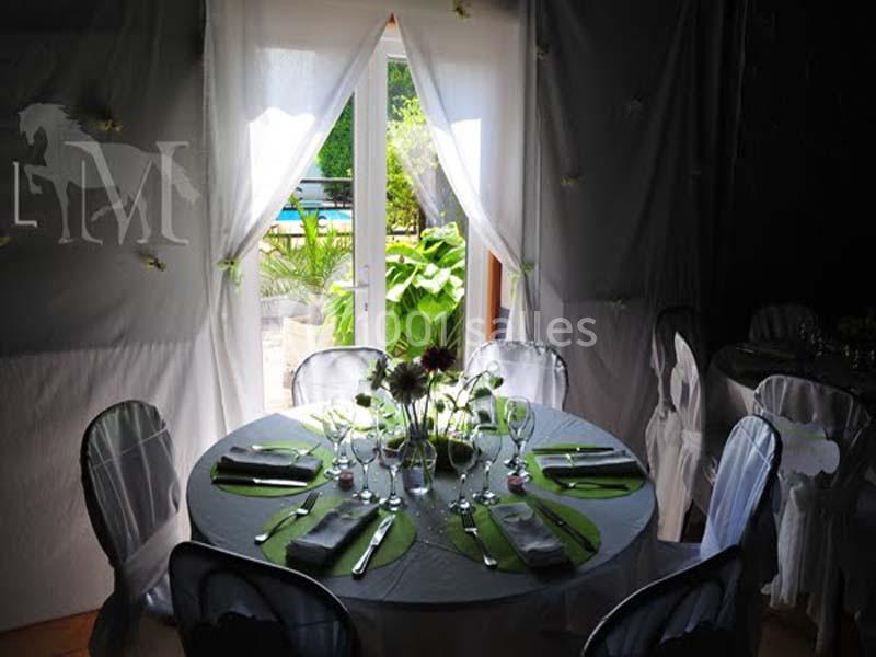 Table ronde décorée avec des couverts et des fleurs, placée près d'une porte ouverte donnant sur un jardin ensoleillé.