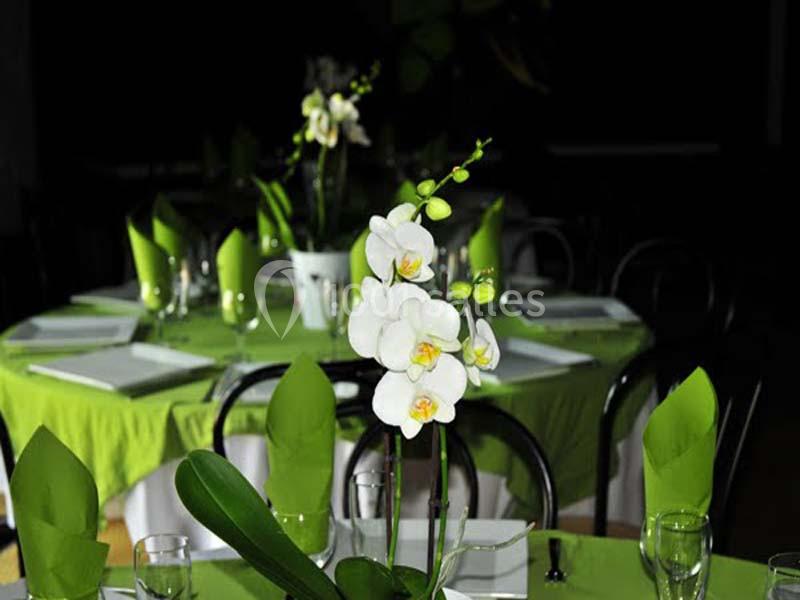 Des tables rondes décorées de nappes vertes, serviettes pliées et une orchidée blanche en premier plan.