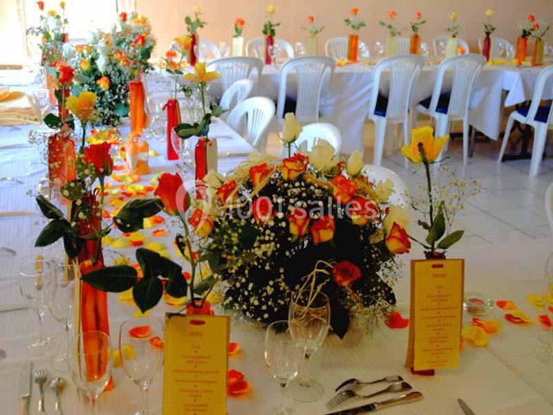 Salle décorée pour un événement avec des tables dressées, des bouquets de fleurs colorées et des menus disposés.
