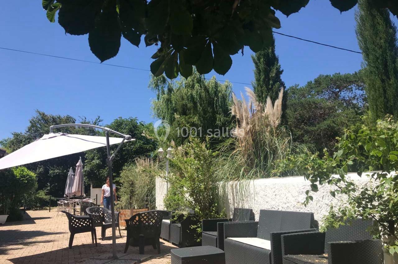 Terrasse ensoleillée avec mobilier de jardin en rotin, parasols ouverts et végétation luxuriante en arrière-plan.