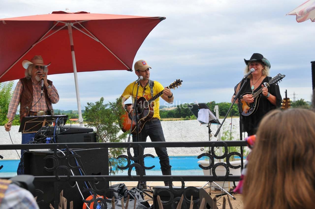Trois musiciens jouent de la musique en plein air sous un parasol rouge, avec des instruments à cordes.