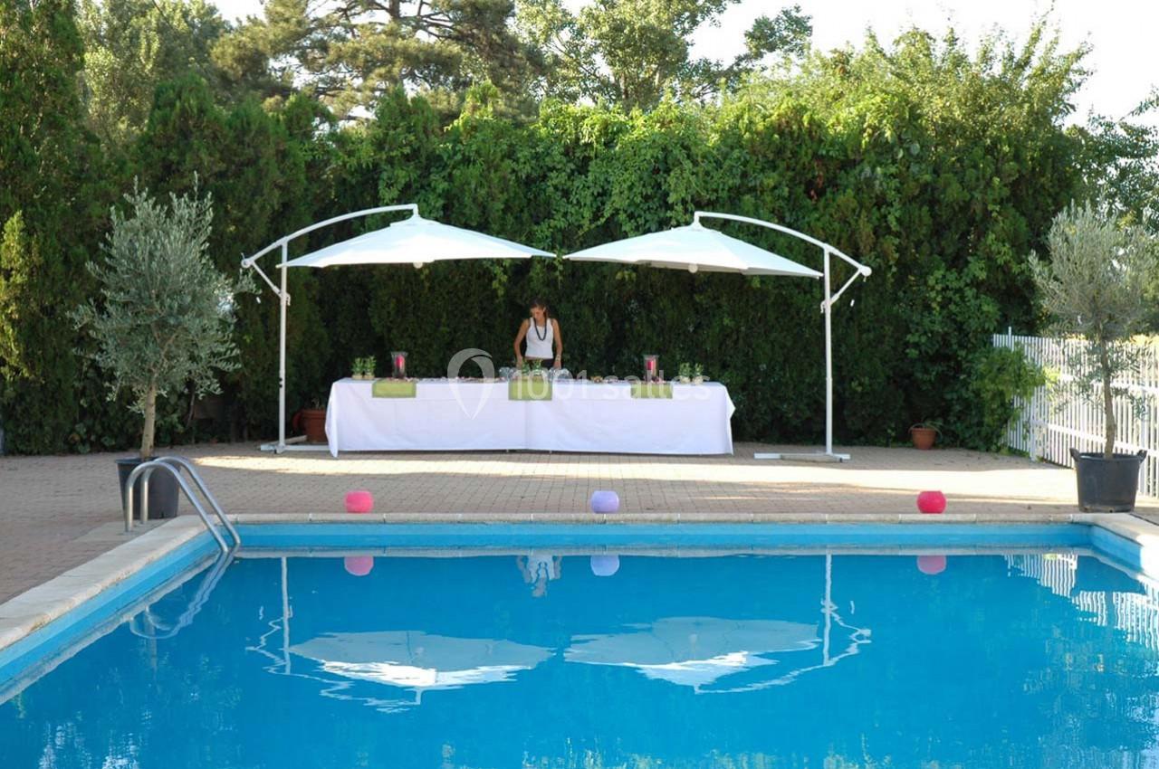 Table dressée sous deux parasols blancs près d'une piscine, entourée de végétation dense en arrière-plan.
