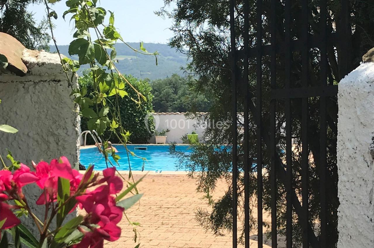 Vue d'une piscine entourée de végétation, visible à travers une porte en fer forgé ouverte.