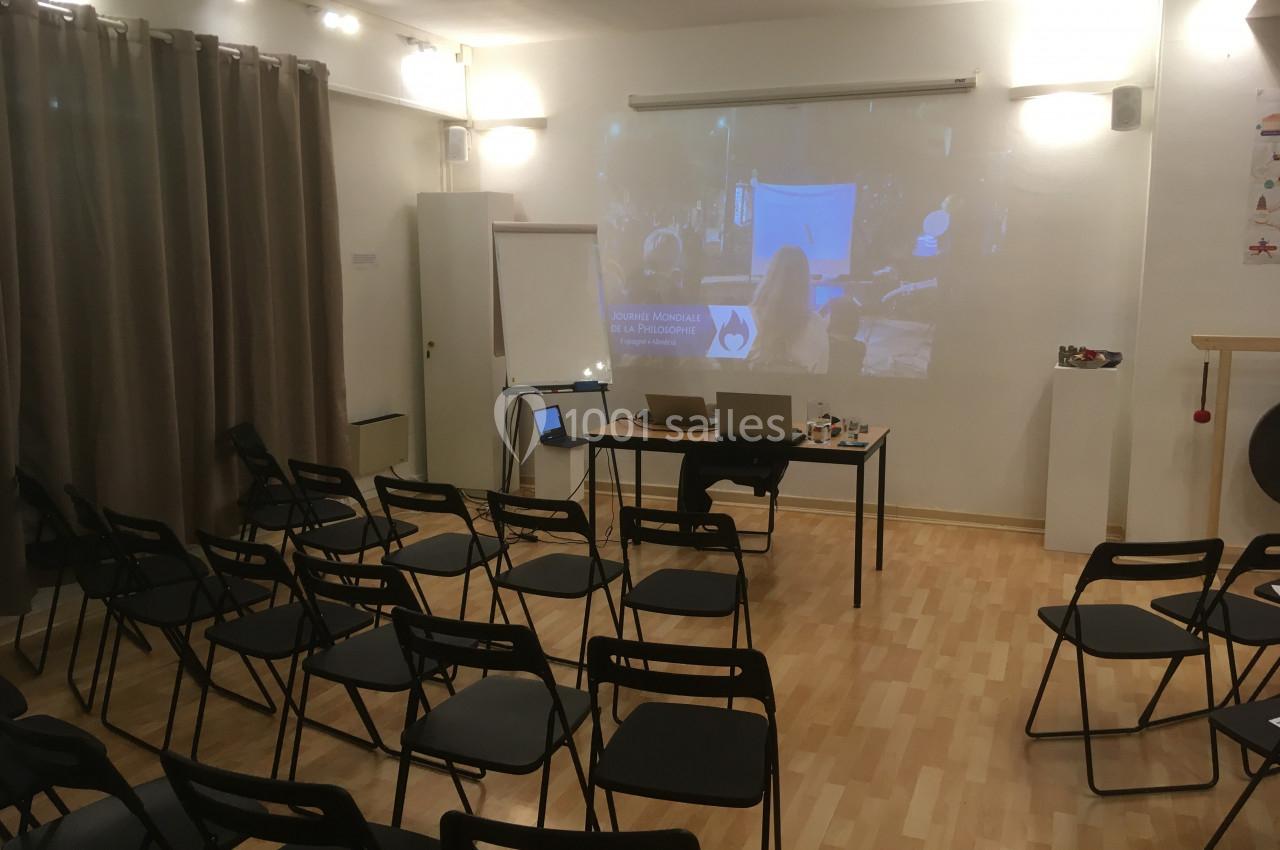 Salle de réunion avec des chaises noires disposées en rangées, un projecteur allumé et un tableau blanc.