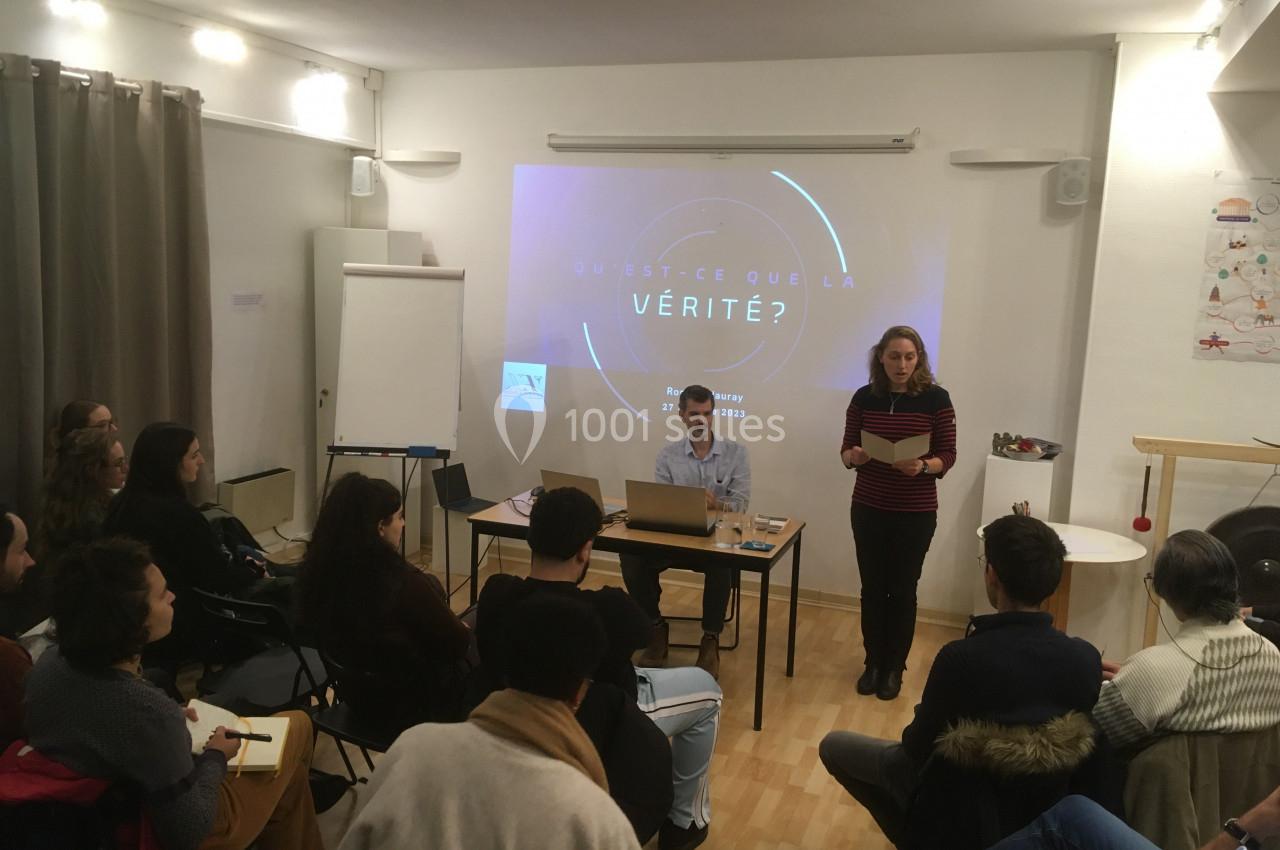Un groupe de personnes assiste à une présentation dans une salle, avec une projection sur le thème de la vérité.