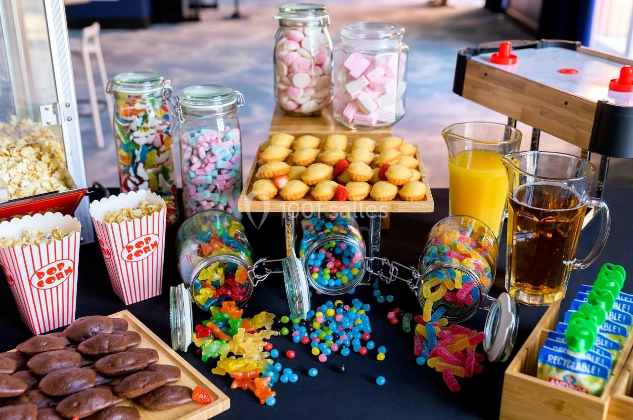 Buffet de friandises avec bonbons, biscuits, popcorn, jus d'orange et thé, présenté sur une table noire.