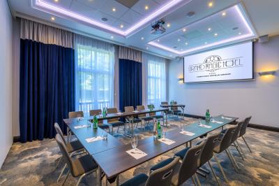 Salle de conférence lumineuse avec rangées de chaises alignées, écran de projection et portes vitrées au fond.