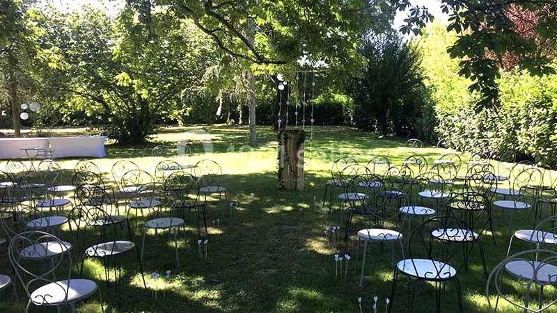 Chaises en métal disposées en extérieur sur une pelouse, entourées d'arbres, avec une décoration centrale.