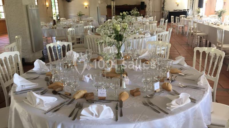 Salle de réception avec tables rondes dressées, nappes blanches, vaisselle élégante et centres de table fleuris.