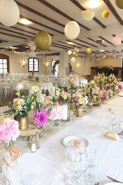 Salle de réception décorée pour un événement, avec des tables ornées de fleurs colorées et des lanternes suspendues.