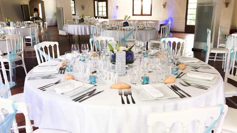 Table ronde élégamment dressée pour un événement, avec nappes blanches, couverts, verres et décorations bleues.