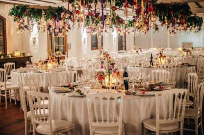 Chaises et tables en fer forgé disposées sous un grand arbre dans un jardin verdoyant, éclairé par la lumière du jour.