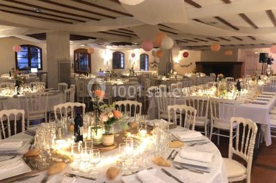 Chaises et tables en fer forgé disposées sous un grand arbre dans un jardin verdoyant, éclairé par la lumière du jour.
