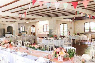 Chaises et tables en fer forgé disposées sous un grand arbre dans un jardin verdoyant, éclairé par la lumière du jour.