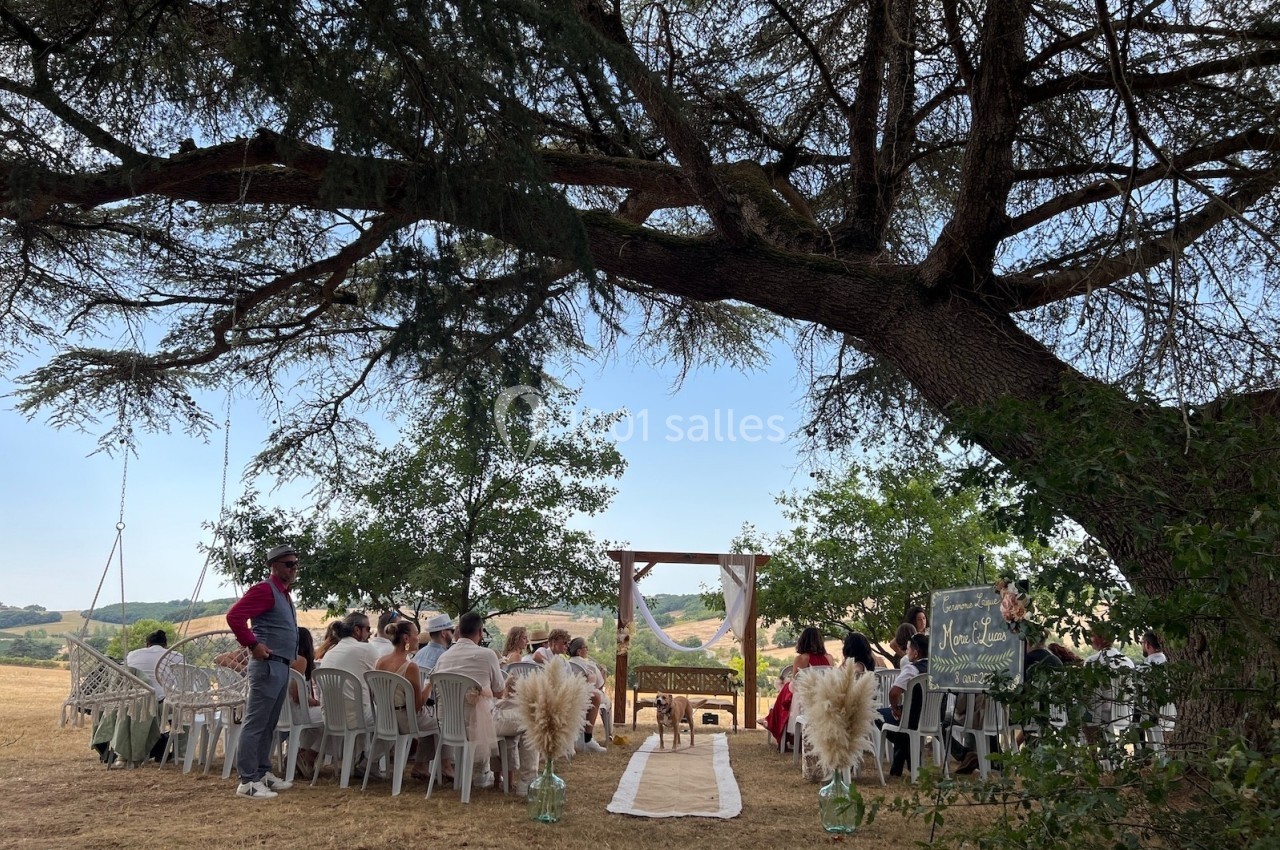 Cérémonie en plein air sous un grand arbre, avec des invités assis face à une arche décorée.