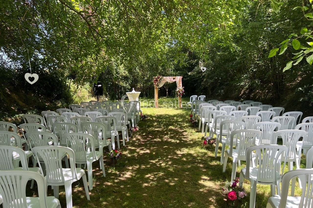 Allée centrale bordée de chaises blanches en plastique, menant à une arche décorée pour une cérémonie en plein air.