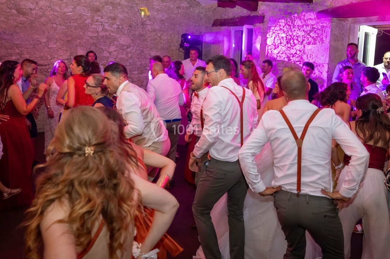 Groupe de personnes dansant lors d'une fête dans une salle en pierre avec éclairage coloré.