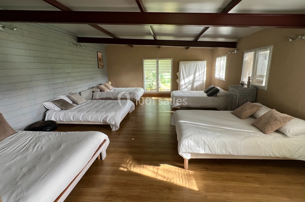 Salle lumineuse avec parquet, équipée de plusieurs lits simples et doubles, décorée de tons neutres.
