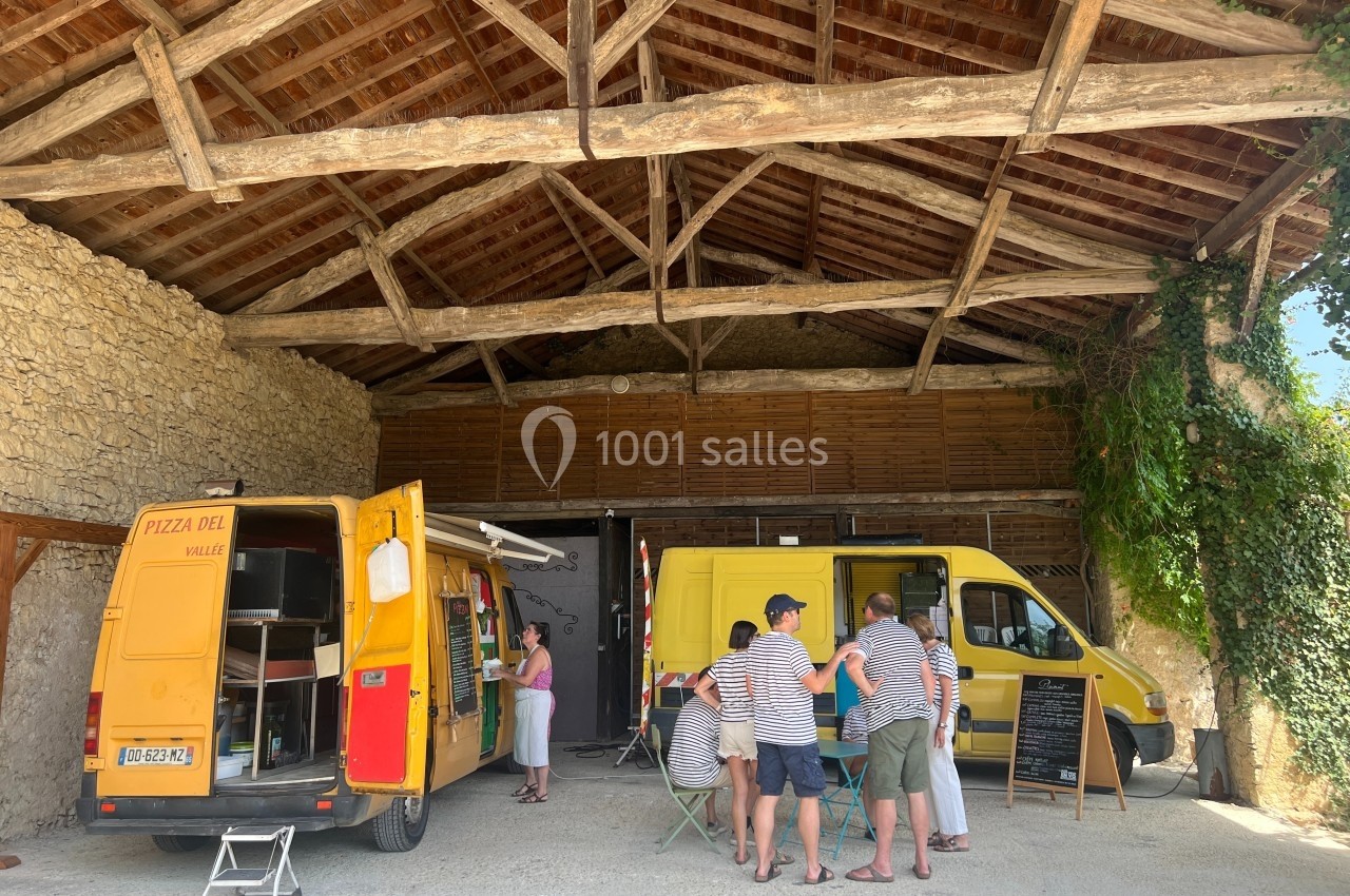 Deux camions jaunes de pizza stationnés sous un hangar en bois, avec des clients attendant leur commande.