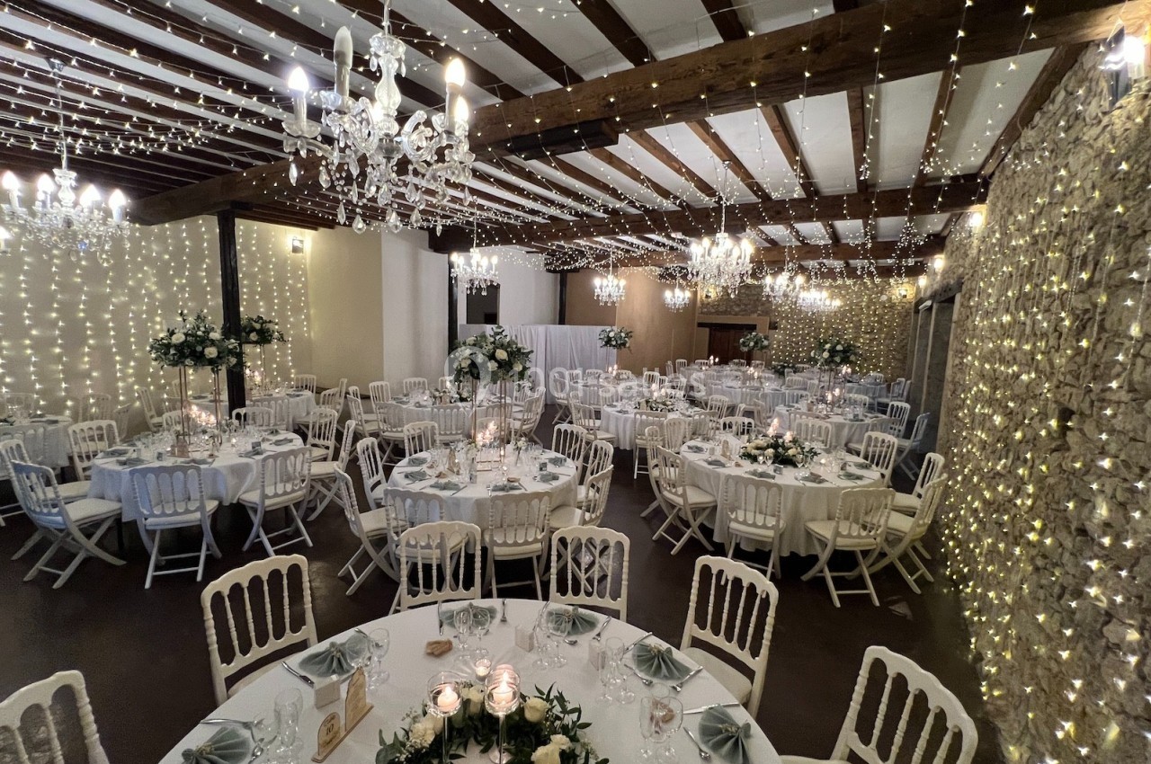 Salle de réception décorée avec des guirlandes lumineuses, des chandeliers et des tables rondes ornées de centres de table…