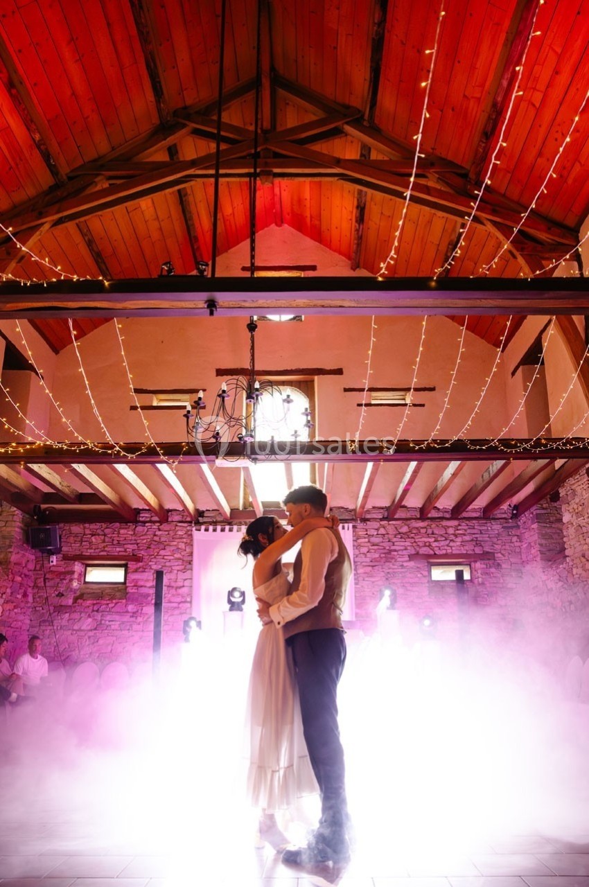 Un couple danse sous un plafond en bois avec des guirlandes lumineuses, entouré de fumée et d'une lumière colorée.