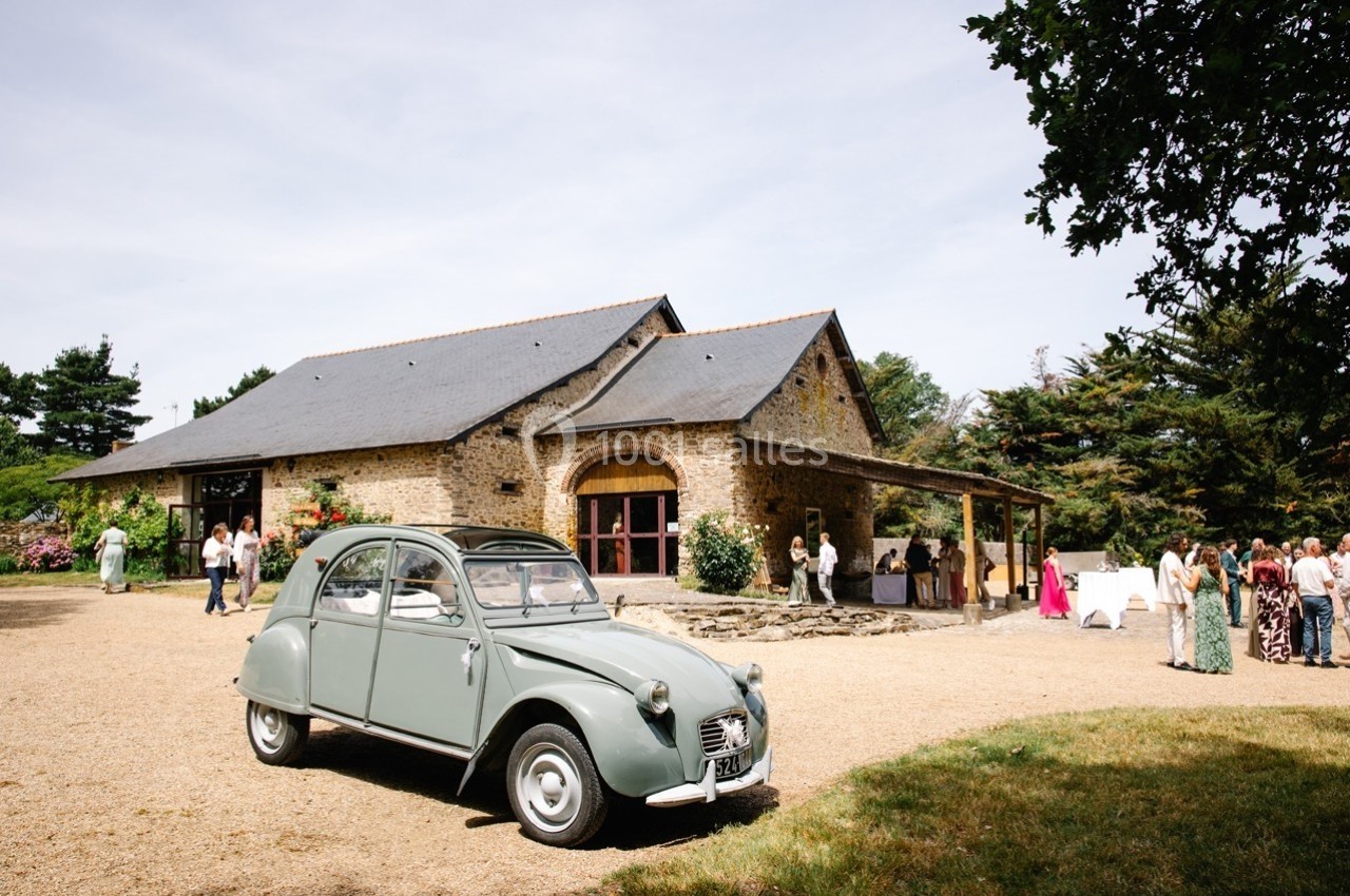 Une voiture ancienne stationnée devant un bâtiment en pierre avec des invités rassemblés à l'extérieur.