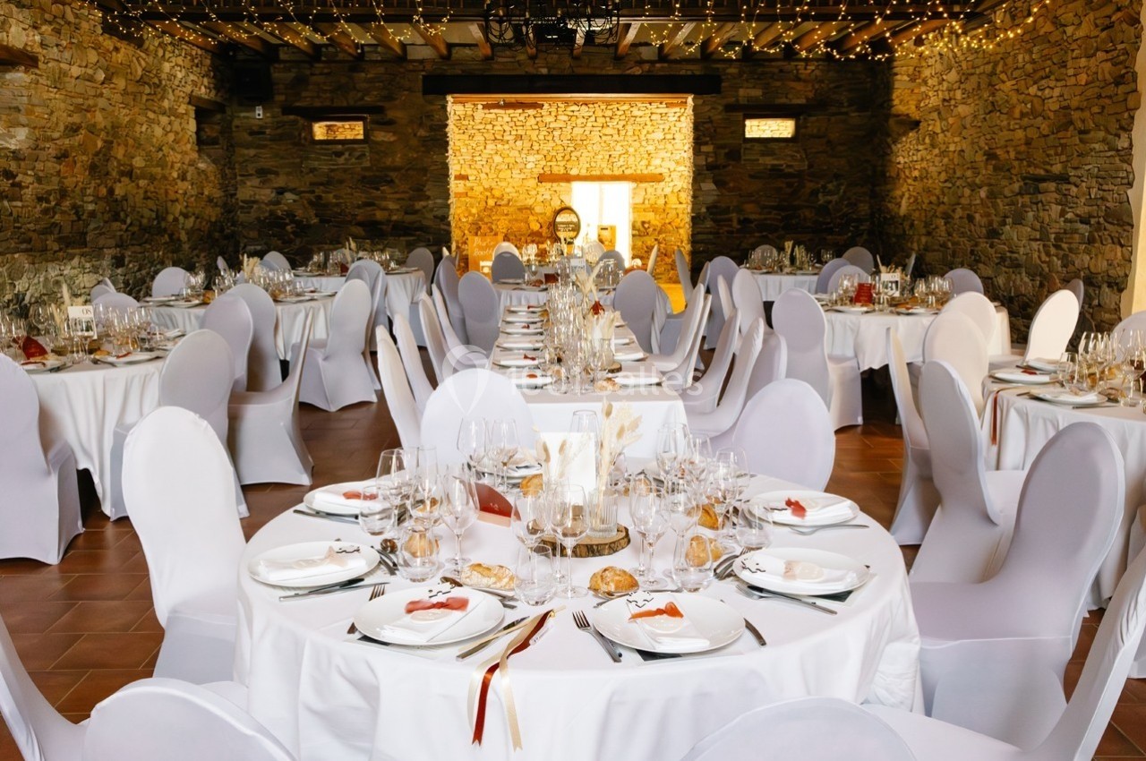 Salle de réception décorée avec des tables rondes dressées, nappes blanches et guirlandes lumineuses suspendues.