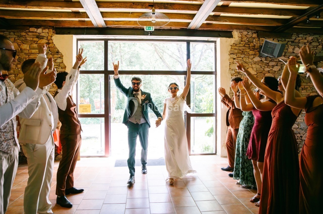Un couple en tenue de mariage entre dans une salle, acclamé par des invités alignés de chaque côté.