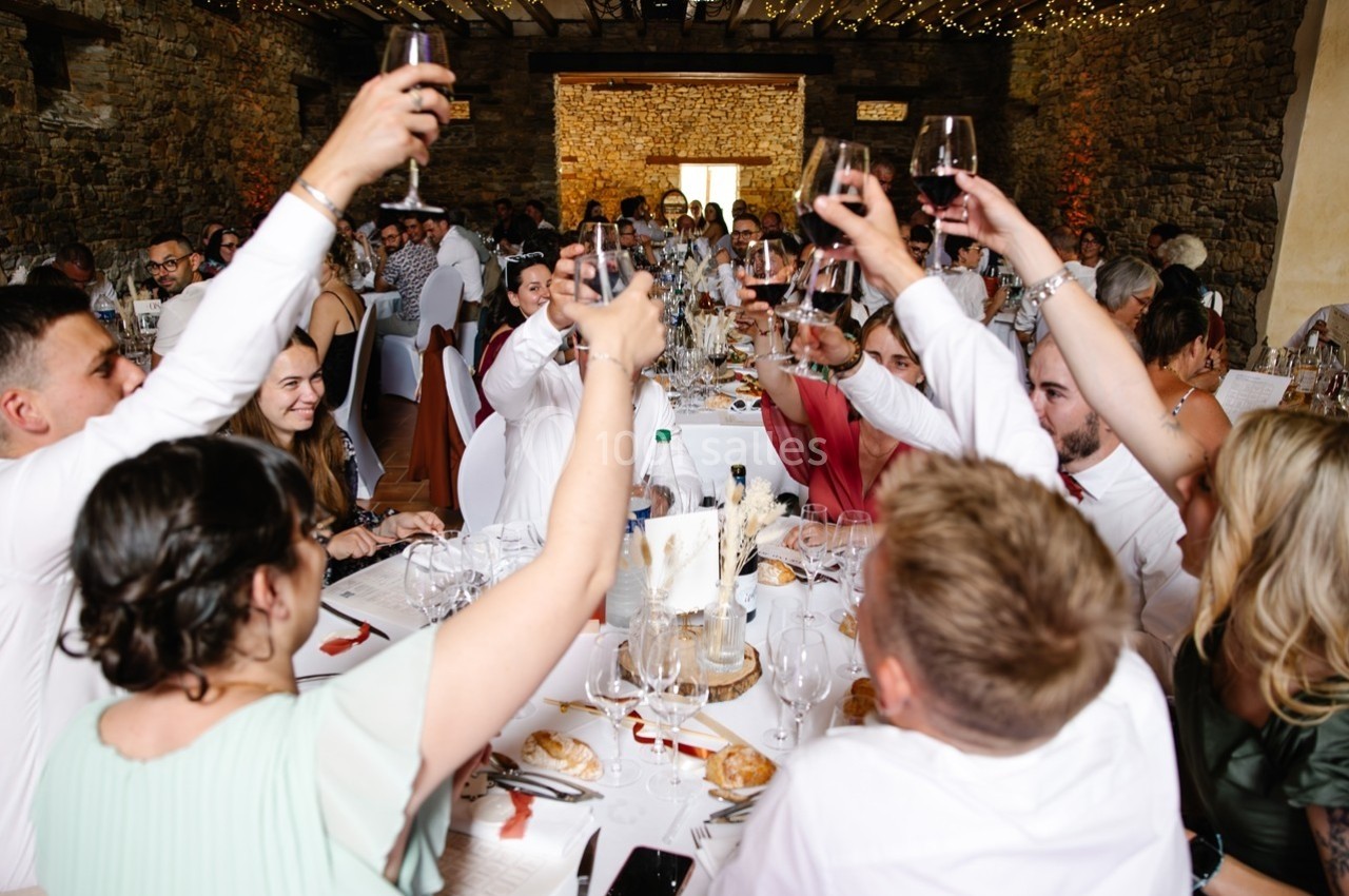 Des convives lèvent leurs verres autour d'une grande table lors d'un repas festif dans une salle en pierre.