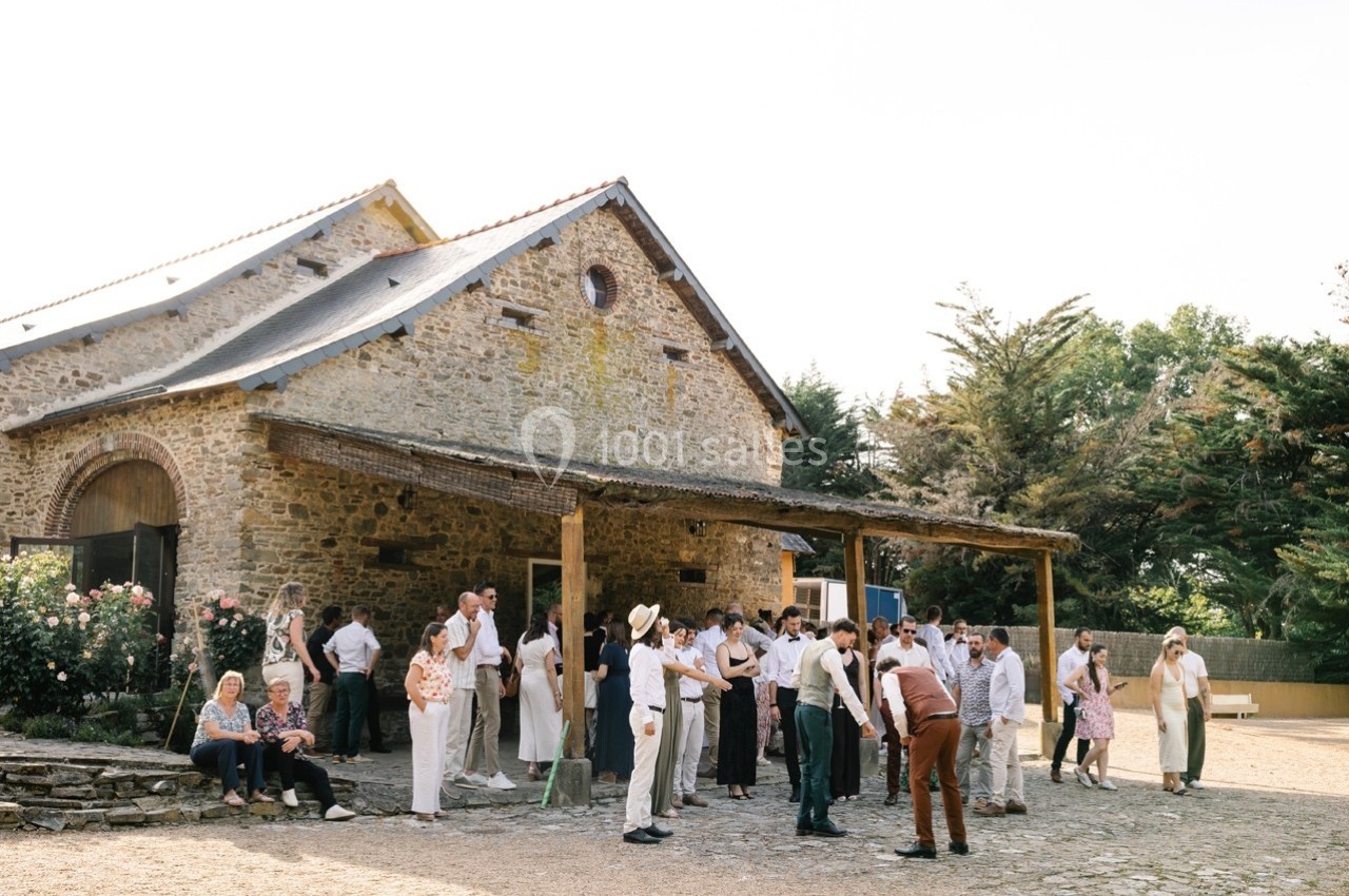 Un groupe de personnes rassemblées devant une grange en pierre dans un cadre extérieur ensoleillé.