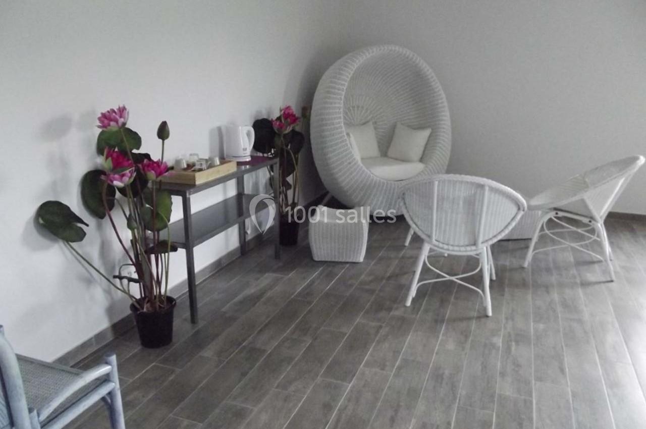 Espace intérieur avec fauteuils en rotin blanc, table d'appoint, plantes et sol en carrelage gris.